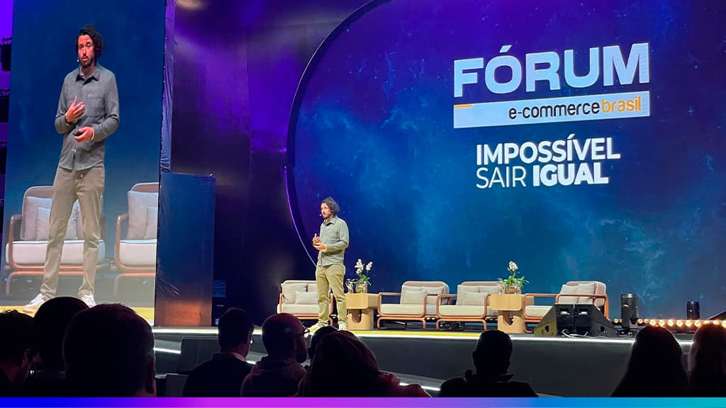 Palestrante em palco no Fórum E-commerce 360, com projeção “Marketing & Vendas” e slogan “Impossível Sair Igual”.