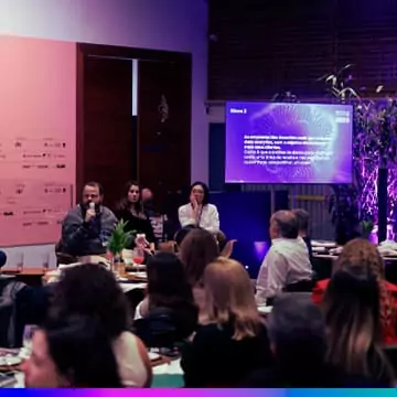 Imagem de uma mesa redonda durante um evento de inovação, com participantes discutindo, enquanto uma apresentação é exibida ao fundo.