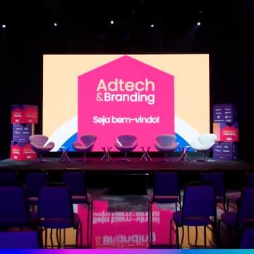 Palco do Adtech & Branding 2025 com telão “Seja bem-vindo!” e cadeiras alinhadas para o painel.