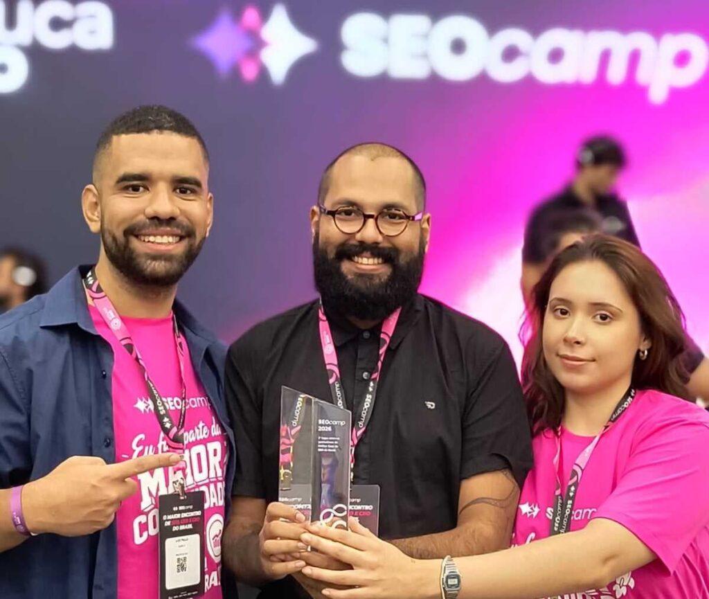 Adonai, Luiz e Jacke posam sorrindo no SEOcamp enquanto seguram o troféu de premiação, celebrando o reconhecimento por um dos melhores cases de SEO do Brasil.