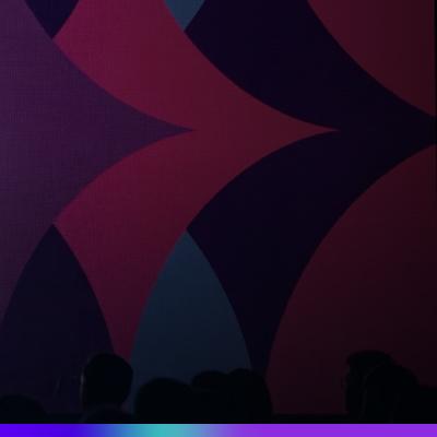 Imagem abstrata com formas geométricas em tons de rosa, roxo e azul escuro ao fundo, com silhuetas de pessoas na parte inferior, representando a atmosfera de um evento.