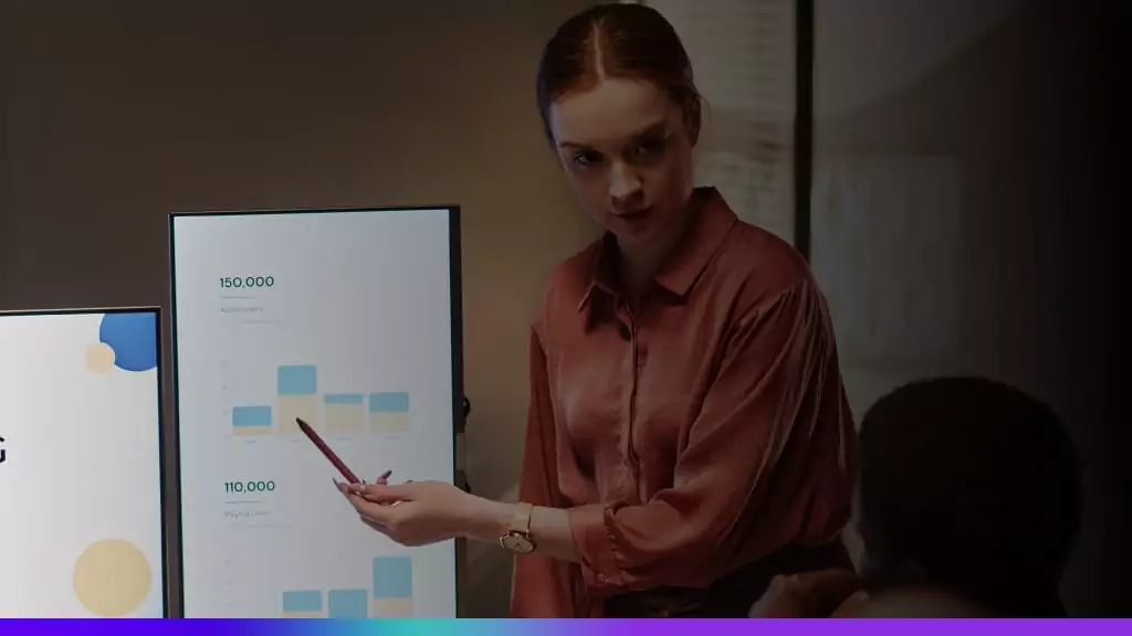 Profissional apresentando gr&aacute;ficos e indicadores em telas durante reuni&atilde;o de an&aacute;lise de m&eacute;tricas de marketing e desempenho de campanhas.
